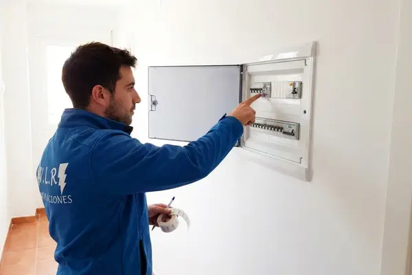 Electricista de VLR Instalaciones señalando los interruptores de un cuadro eléctrico abierto en el pasillo de una vivienda