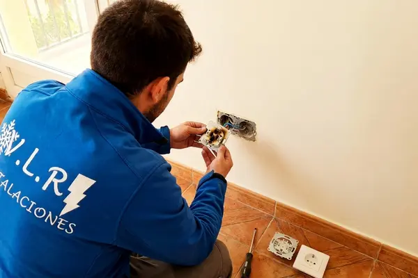 Electricista de VLR Instalaciones examinando el mecanismo quemado de un enchufe que acaba de desmontar de la pared