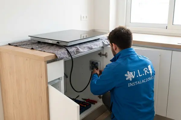 Electricista de VLR Instalaciones conectando una placa de inducción al punto de conexión dentro del mueble de cocina