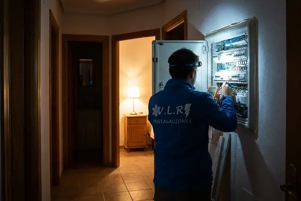 Electricista de VLR Instalaciones revisando de noche un cuadro eléctrico con frontal y multímetro en el pasillo de una vivienda